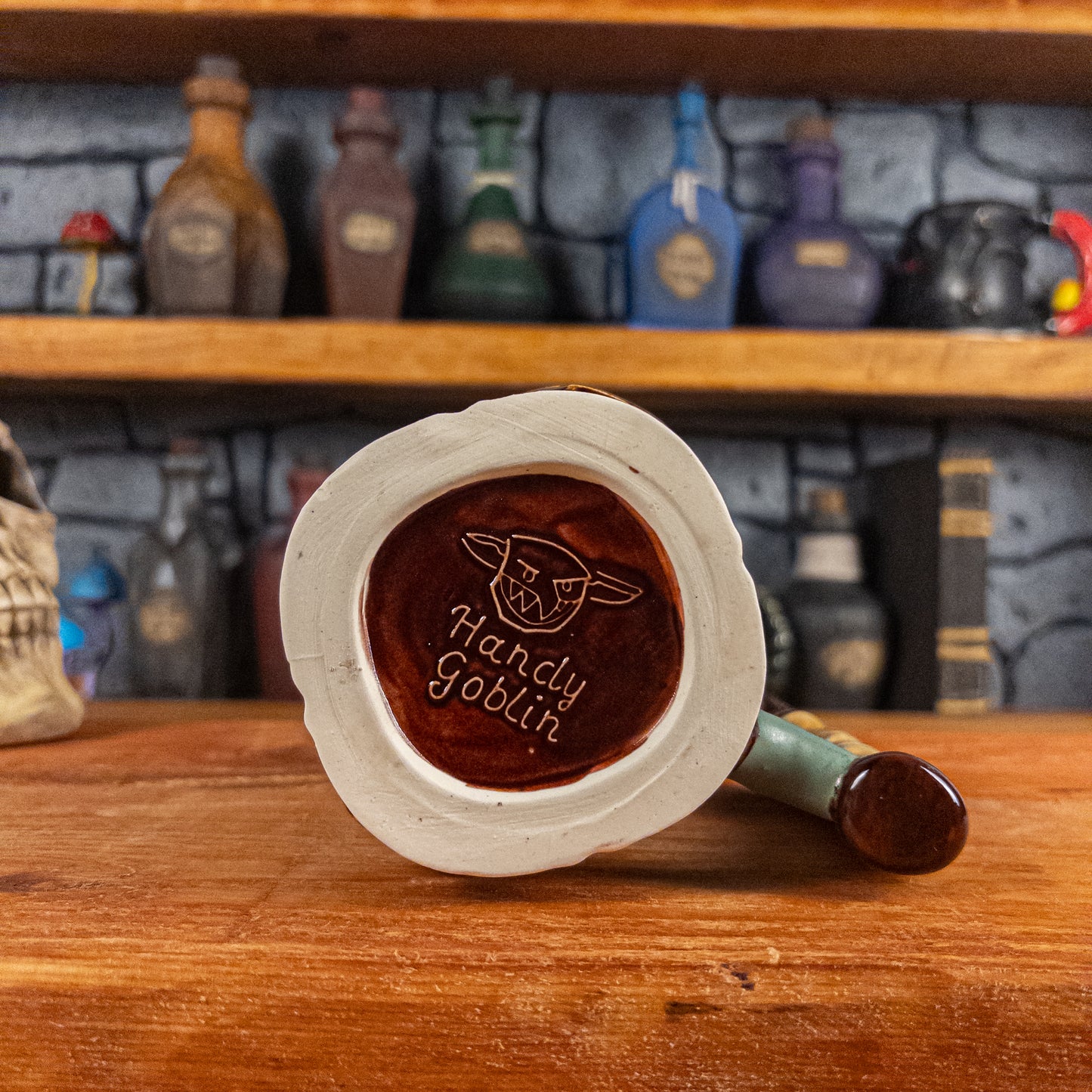 Bottom view of a handmade Dwarven Mug with the 'Handy Goblin' logo embossed in the center, featuring a dark red base.